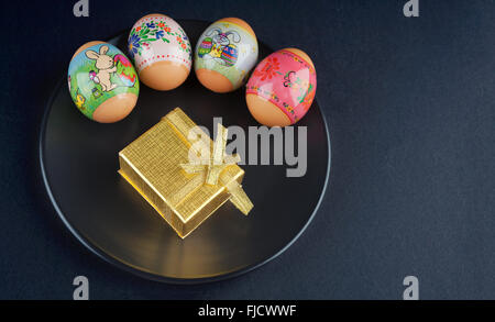 Four colored Easter eggs and a golden gift box on black plate Stock Photo