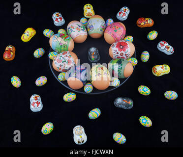 Easter eggs with beautiful ornaments and foil-wrapped chocolate eggs scattered with easter bunny on a black plate. Stock Photo