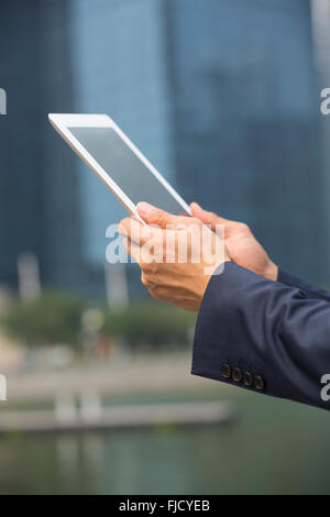 Close-up view of an Asian businessman using digital tablet outside modern office building. Stock Photo