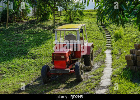 old red tractor, parked on the green grass. The brakes are uncertain, so there's been a rock at one wheel, so it does not roll d Stock Photo