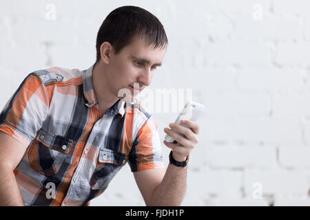 Portrait of casual young man holding mobile phone, using smartphone app, looking at screen reading or sending text message Stock Photo