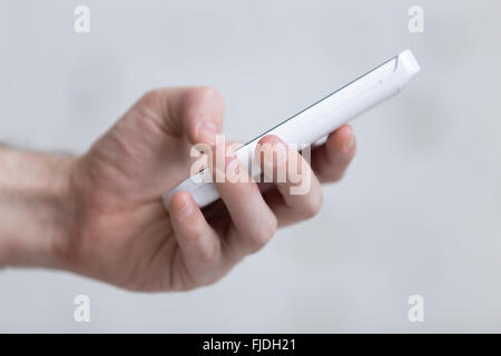 Young man holding white mobile phone in hand, dialling a number, using smartphone app, close-up Stock Photo