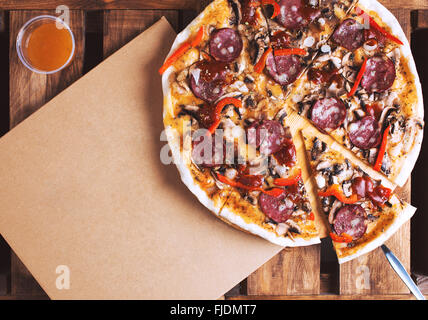 Flat lay shot of delicious italian pizza with meat and vegetables and cardboard delivery box. Pizza delivery service. Stock Photo