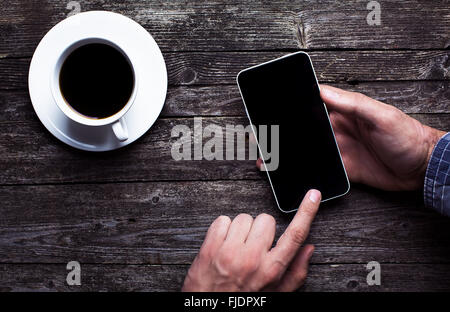 Male hands in shirt using smartphone with large blank touchscreen on dark rustic wood with a cup of coffee. Avobe view flat lay Stock Photo