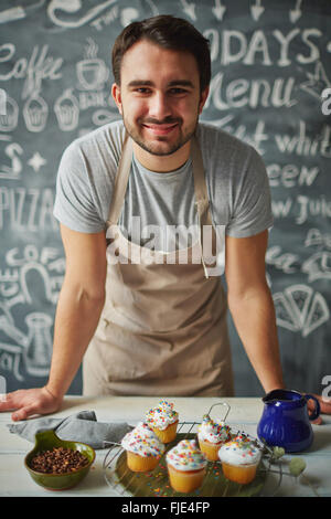 Happy chef looking at camera behind counter of desserts Stock Photo