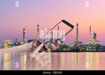 double exposure of female hand hold and touch screen smart phone, on oil refinery blurred background. Stock Photo