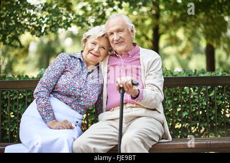 Happy mature couple sitting on bench in the park Stock Photo