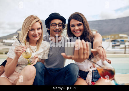 Group of friends taking selfie on a smart phone. Young man and women with drinks taking a self portrait on cell phone. Young peo Stock Photo