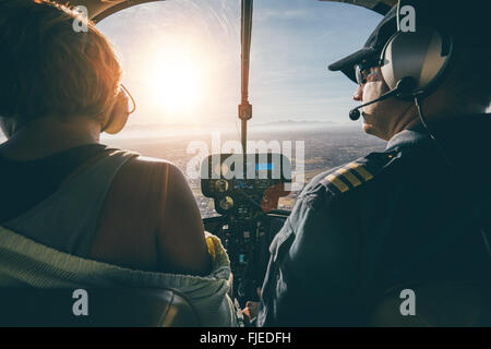 Rear view of male and female pilots flying a helicopter on sunny day. Man flying a helicopter with his copilot looking outside t Stock Photo