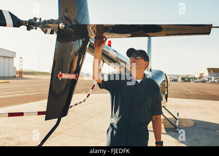 Male pilot in uniform examining helicopter tail wing. Pre flight inspection by pilot at the airport. Stock Photo