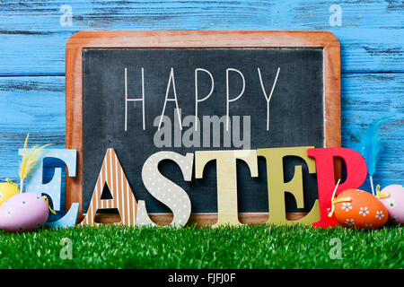 some decorated eggs on the grass, and the text happy written in a chalkboard and three dimensional letters forming the word east Stock Photo