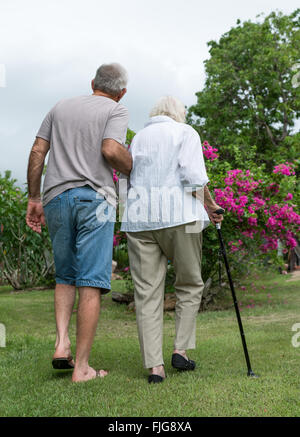 Man helping elderly lady with walking cane in garden Stock Photo