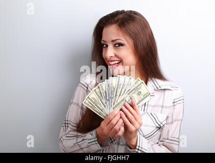 Happy successful young woman holding dollars in hands with toothy smiling on blue background Stock Photo