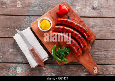 Grilled sausage on a wooden board with sauce and vegetables Stock Photo