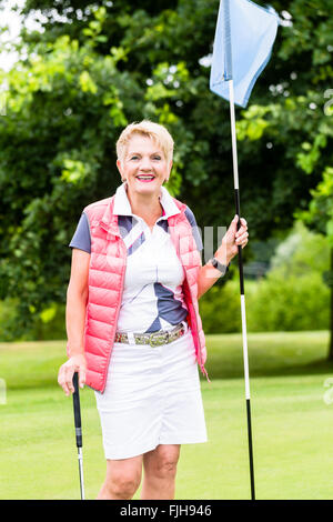 Senior woman playing golf on course holding flag Stock Photo