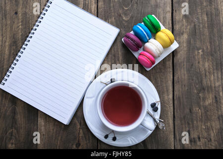 White notebook on wooden table with cup of tea and colorful macaroons Stock Photo