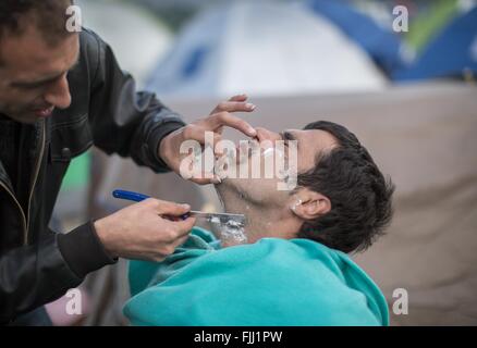 Idomeni, Greece. 2nd Mar, 2016. A barber from Syria has set up his mobile barber's shop and shaves a customer, at the refugee camp at the border between Greece and Macedonia, in Idomeni, Greece, 2 March 2016. Since Monday, Macedonia is barely letting in any refugees. A massive camp with thousands of refugees has formed at the border crossing in Idomeni. PHOTO: MICHAEL KAPPELER/DPA/Alamy Live News Stock Photo