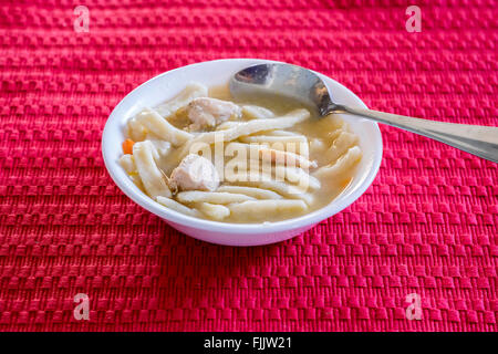 A white bowl full of homemade chicken and noodles on a red placemat. Oklahoma, USA. Stock Photo