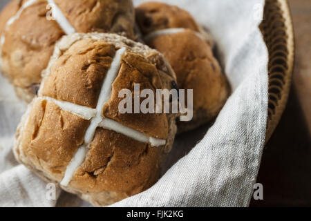 Three Easter hot cross buns in a basket on a rustic wooden table Stock Photo