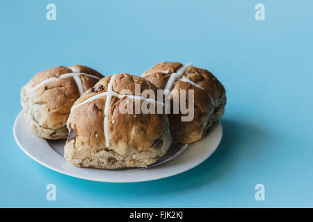 Three Easter hot cross buns on a white plate on a blue background Stock Photo