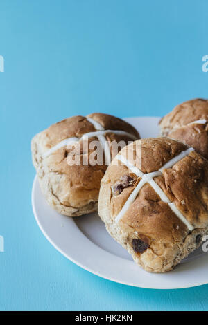 Three Easter hot cross buns on a white plate on a blue background Stock Photo