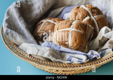 Three Easter hot cross buns in a basket with blue and grey linen cloth Stock Photo