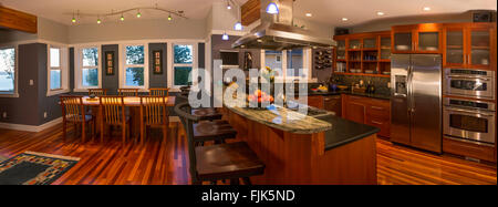 Open plan kitchen & dining area in contemporary upscale home interior with wood cabinets and floors, view windows, appliances and breakfast bar Stock Photo