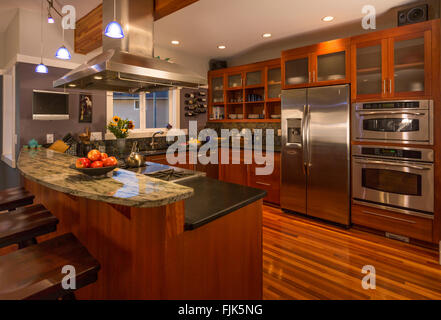Contemporary upscale home kitchen interior with wood cabinets & floors, granite countertops, stainless steel appliances and accent lighting Stock Photo