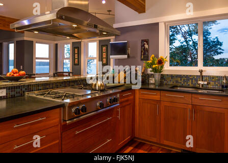Contemporary upscale home kitchen interior with custom wood cabinets, gas stove, stainless steel vent hood, mosaic tile backsplash and view windows Stock Photo