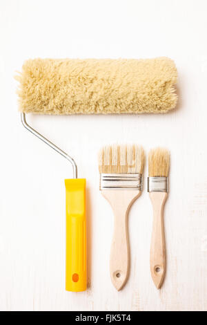 Two paint brushes and roller on white wooden background