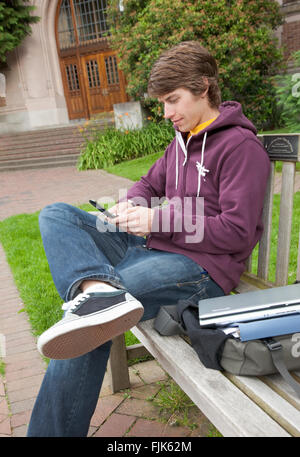 Male college student with cell phone on campus. He is looking at it as if texting, checking email or surfing the internet. Stock Photo