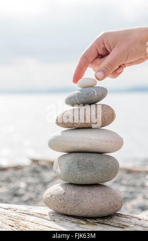 Woman's hand balancing a stack of stones on a sunny beach. Beautiful nature, balance, health, wellness concepts. Stock Photo