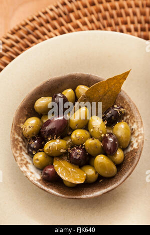 Mediterranean style appetizer of French green picholine and Greek black kalamata olives with bay leaves & dried herbs in serving dish Stock Photo