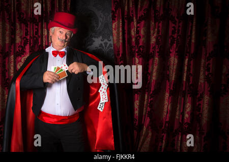 Mature magician on stage performing a magic trick with cards Stock Photo