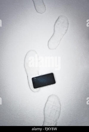 Someone stepped on  a phone and damaged screen. Device in snow with foot imprints. Stock Photo