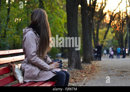 Girl sitting on the bench in park in the evening Stock Photo
