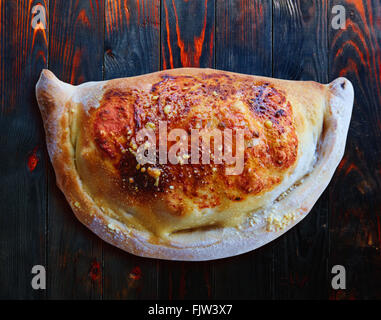 Pizza Calzone folded as a patty on a wooden board table Stock Photo