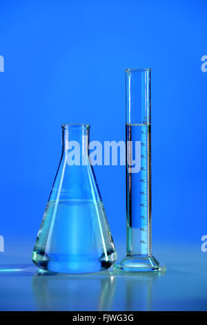 Laboratory flask and graduated cylinder with blue light over table Stock Photo