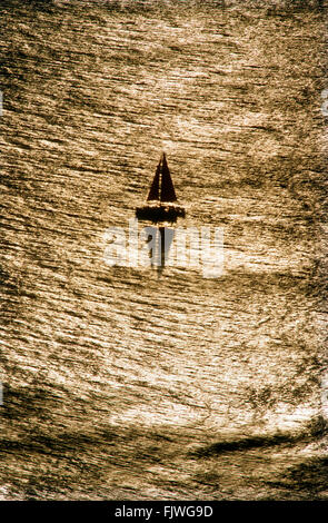 Lone sailboat on calm Pacific Ocean off California coast with sun reflecting across shinning surface