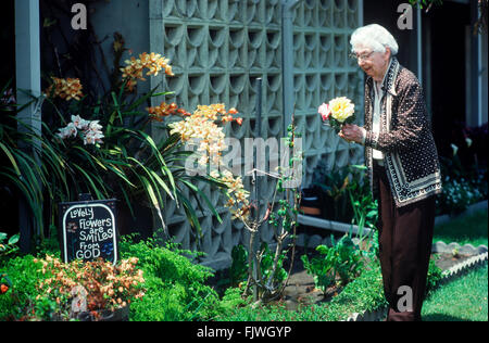 95 year old Grandmother in her rose garden at Leisure World in California with symbolic words on sign Stock Photo