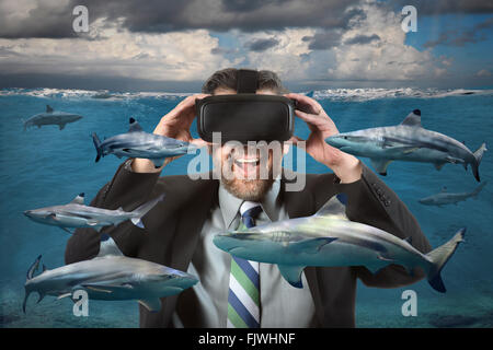 Businessman seeing sharks in the ocean using virtual reality glasses Stock Photo