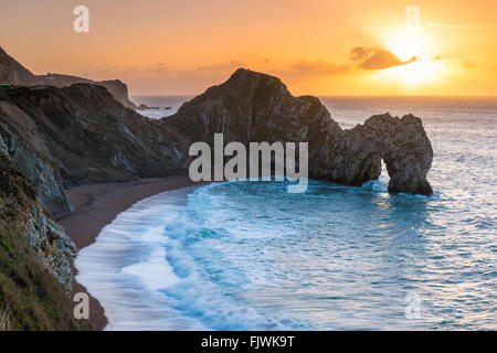 The rising sun on a winters morning seen over the limestone arch of Durdle Door on the Jurassic Coast of Dorset, UK