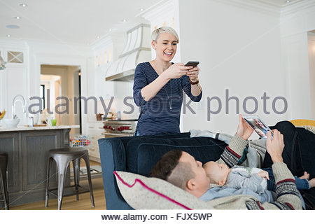 Mother photographing husband and baby son on sofa