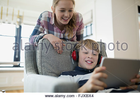 Sister watching brother with headphones using digital tablet