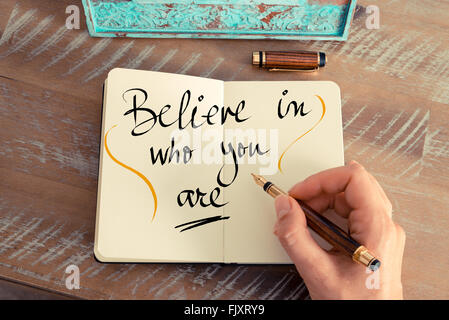 Retro effect and toned image of a woman hand writing a note with a fountain pen on a notebook. Handwritten text Believe in Who You Are as business concept image Stock Photo