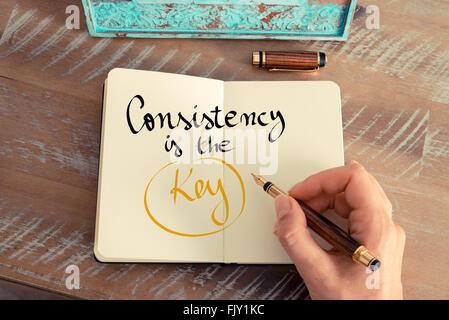 Retro effect and toned image of a woman hand writing a note with a fountain pen on a notebook. Handwritten text Consistency is the Key as business concept image Stock Photo