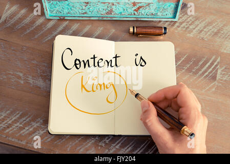 Retro effect and toned image of a woman hand writing a note with a fountain pen on a notebook. Handwritten text Content is King as business concept image Stock Photo