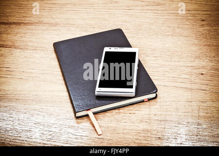 Black leather business diary and Mobile phone on wood table background, Vintage color filter. Stock Photo