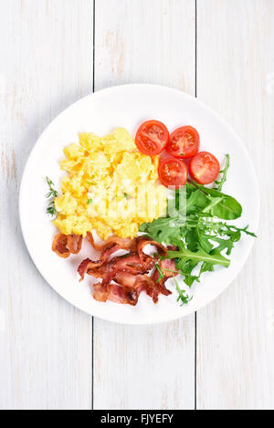 Scrambled eggs, bacon and vegetable salad on plate, top view Stock Photo