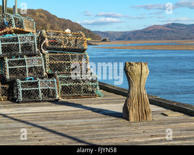 Old wooden bollard on a jetty near lobster pots and the distant wooded mountainsides of the Dyfi estuary. Stock Photo